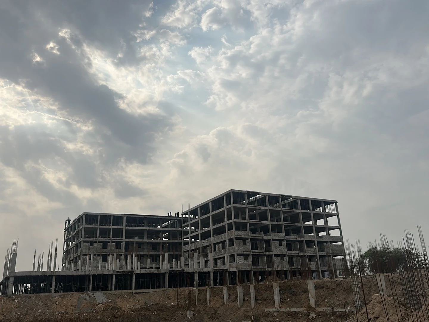On-site photograph of two Fortune Towers blocks under construction, seen from below against a partly cloudy sky: bare R.C.C. frame with exposed rebar at roof level, six-plus storeys, rows of vertical rebar columns for an adjacent block in the foreground.